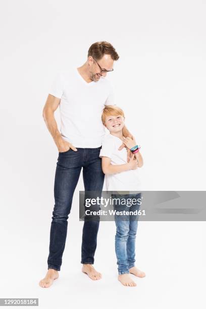 smiling father looking at son while standing against white background - kids standing stock-fotos und bilder