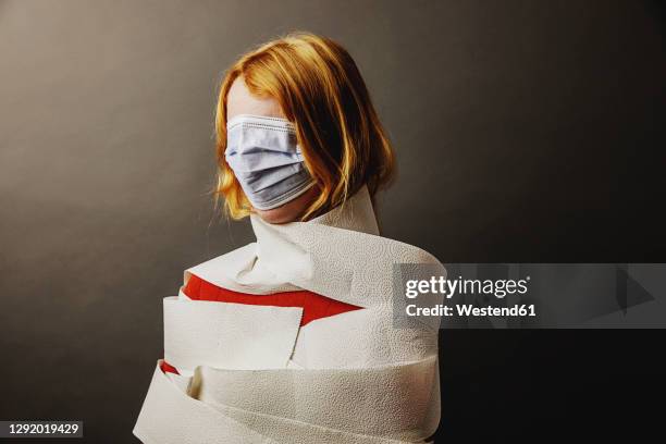 teenage girl wrapped in toilet paper and face covered with protective face mask standing against gray background - wrapped in toilet paper stock-fotos und bilder