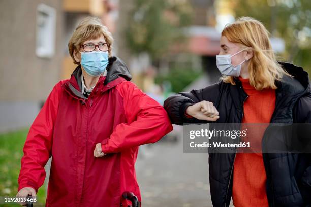 granddaughter and mother wearing face mask greeting with elbow bump while standing outdoors - elbow greeting stock pictures, royalty-free photos & images