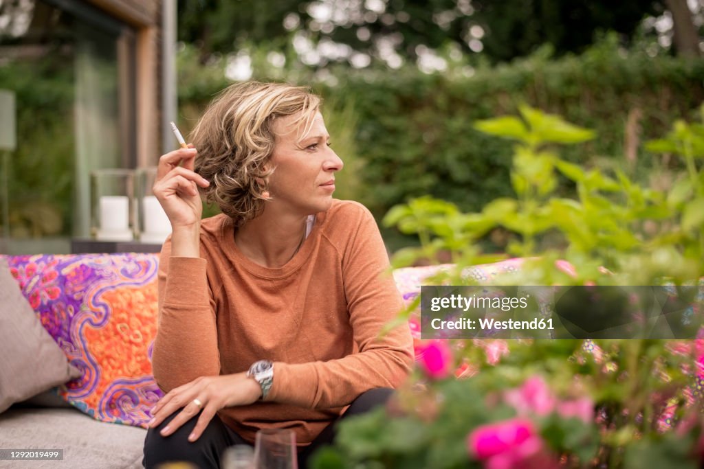 Woman holding cigarette while sitting on sofa at backyard