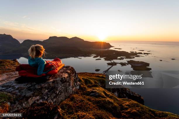 hiker admiring sunset view while lying in sleeping bag at volandstinden, lofoten - couché de soleil photos et images de collection