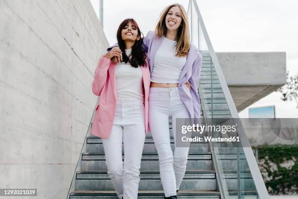 happy sibling with arms around moving down steps in city - blazer viola foto e immagini stock