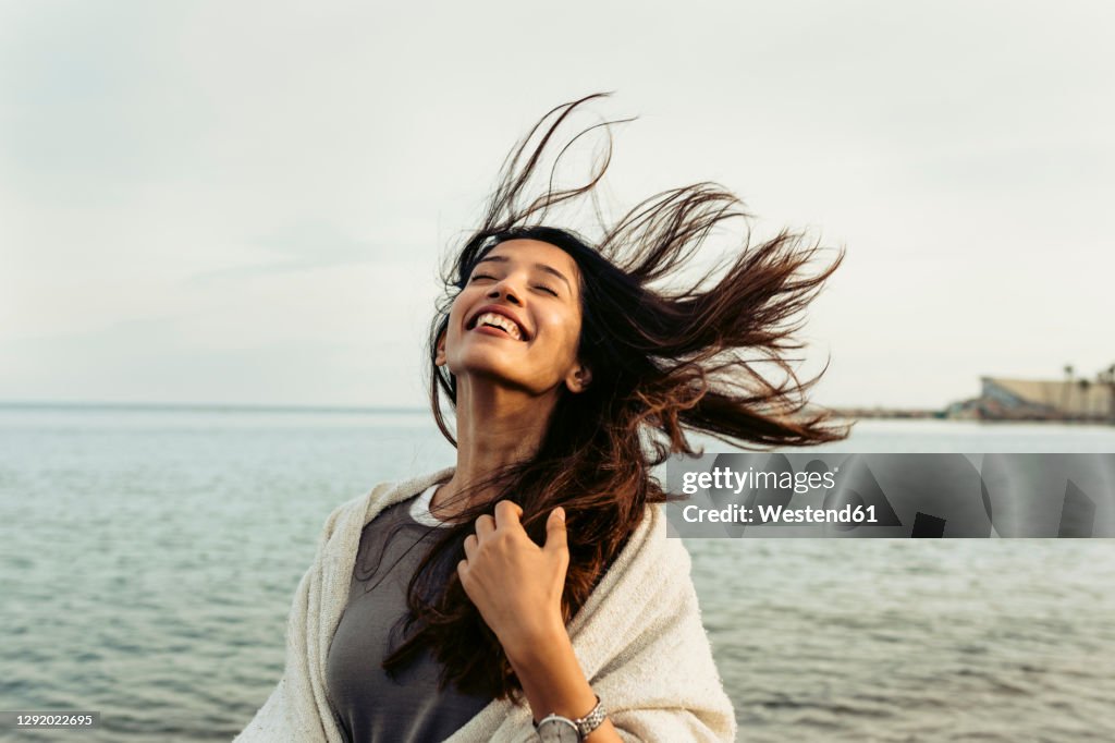 Carefree woman with tousled hair against sky at beach