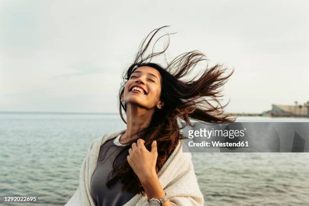 carefree woman with tousled hair against sky at beach - vento foto e immagini stock
