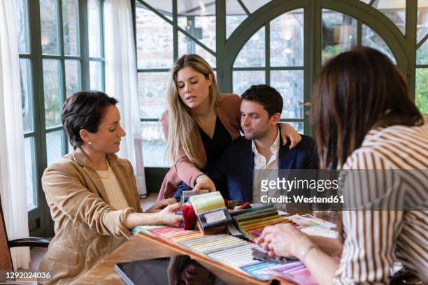couple choosing colorful fabric swatches with their female wedding planners in studio - event planning stock pictures, royalty-free photos & images