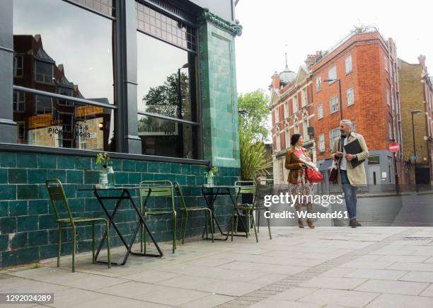 male and female coworkers talking while walking on footpath in city - pavement cafe - fotografias e filmes do acervo