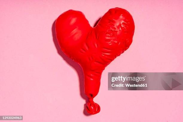 studio shot of red heart shaped deflated balloon - deflated stock-fotos und bilder