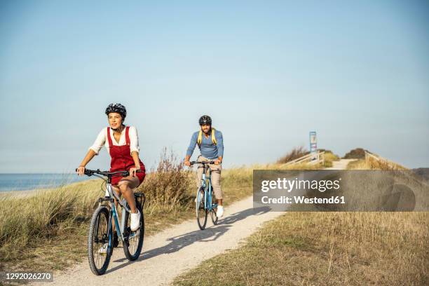 young man and woman wearing cycling helmet riding bicycles on sunny day - cycling helmet stock pictures, royalty-free photos & images