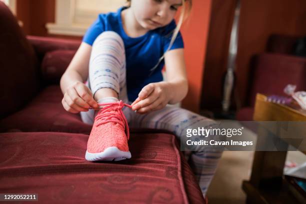 young girl sitting on sofa and tying a shoe lace on her sneaker - fingertier stock pictures, royalty-free photos & images