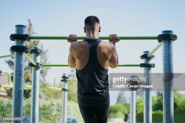 back view of a man practicing calisthenics in a park on sunny day - back stretch stockfoto's en -beelden