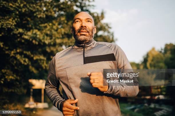 confident man looking away while jogging in park during sunset - jogging stock-fotos und bilder