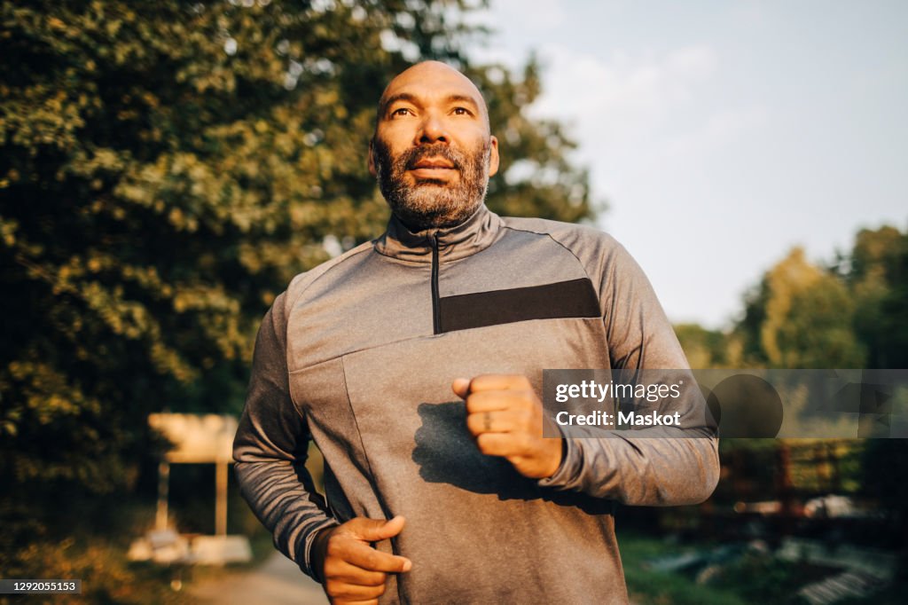 Confident man looking away while jogging in park during sunset