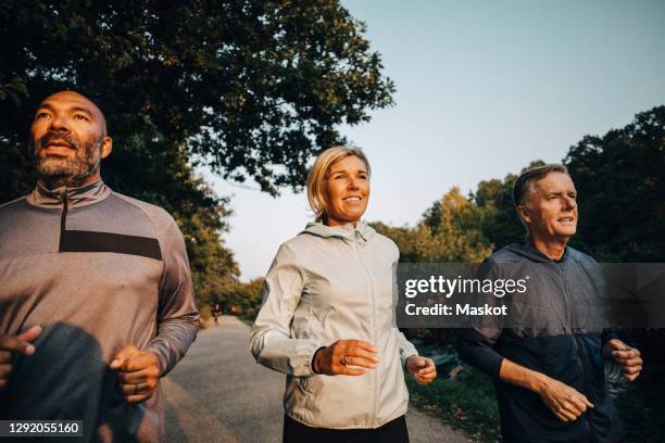 smiling female with friends looking away while jogging in park during sunset - oefenen stockfoto's en -beelden