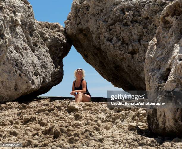 woman sitting by large rocks, ras il-qammieh , mellieha, malta - malta wandern stock-fotos und bilder