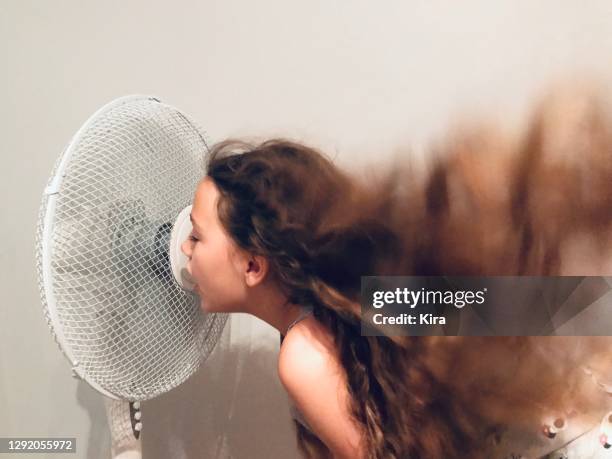 girl with long hair standing in front of a fan cooling down - heatwave stockfoto's en -beelden