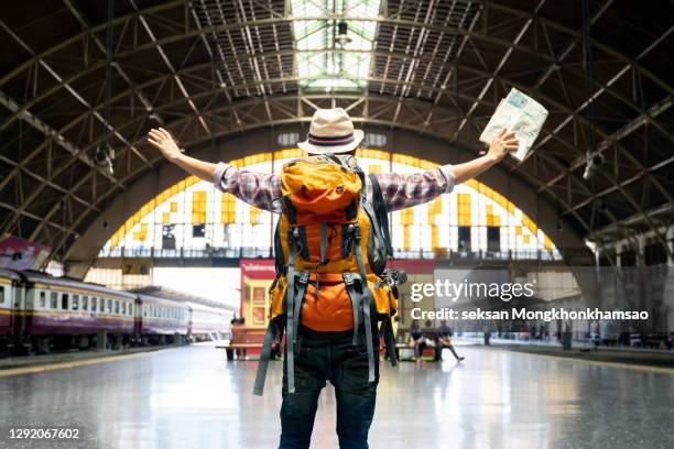 back view of an asian backpacker standing at a train station. travel lifestyle concept - viaje barato fotografías e imágenes de stock