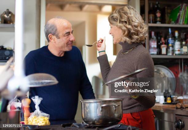 woman making a hearty soup, having her husband taste from spoon - middle aged couple cooking ス�トックフォトと画像