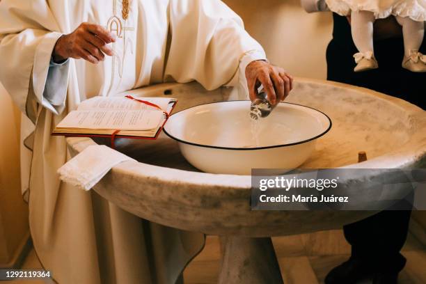 priest throws the sacred water into the baptismal font during a baby's baptism - pila bautismal fotografías e imágenes de stock