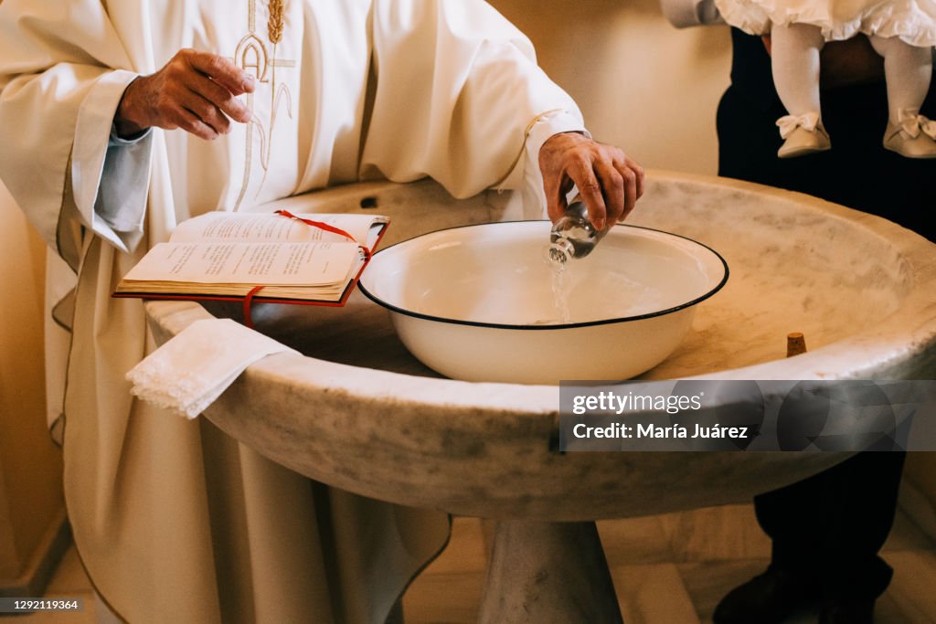 Priest throws the sacred water into the baptismal font during a baby's baptism