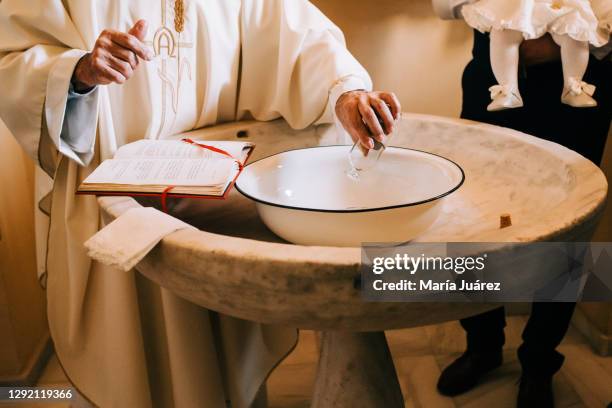 priest throws the sacred water into the baptismal font during a baby's baptism - dopen stockfoto's en -beelden