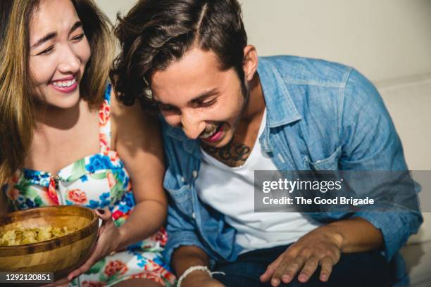 cheerful young friends laughing while sitting on sofa during party - hysteria imagens e fotografias de stock