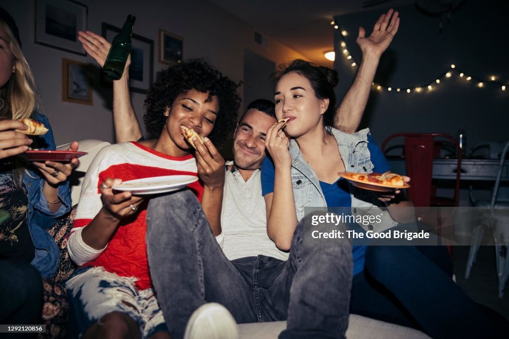 Friends eating pizza on sofa during party at home
