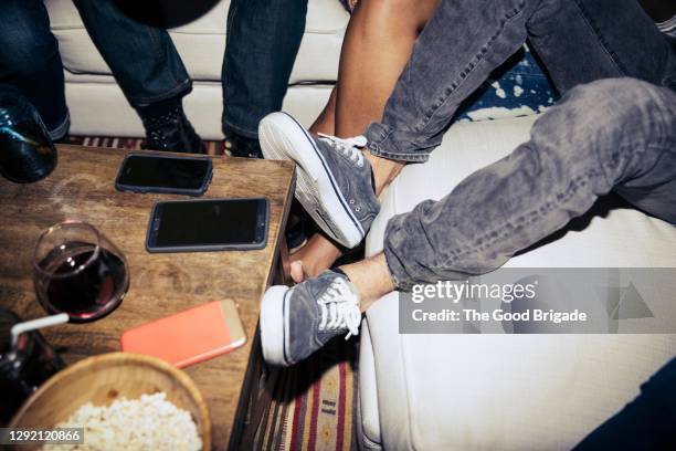 low section of friends sitting on sofa by coffee table in living room - schuhe frau von oben stock-fotos und bilder