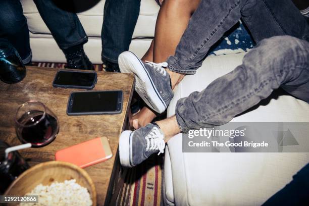 low section of friends sitting on sofa by coffee table in living room - table leg stock pictures, royalty-free photos & images