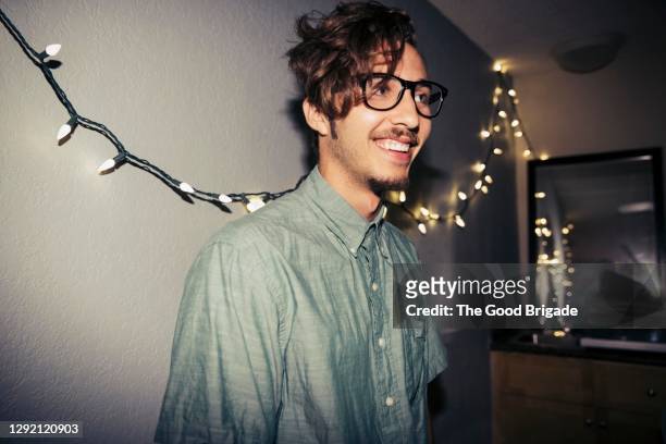 smiling handsome young man looking away while standing against  wall at home - homme hipster stock-fotos und bilder