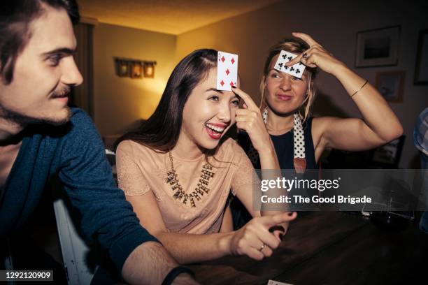 cheerful women with playing cards on forehead during party - game house stock-fotos und bilder