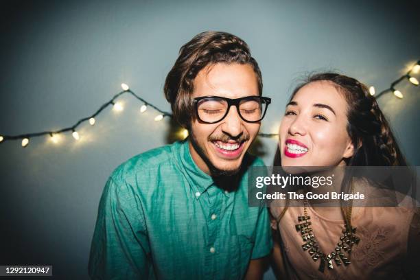 portrait of smiling young woman with male friend enjoying party against wall at home - the party inside stock pictures, royalty-free photos & images