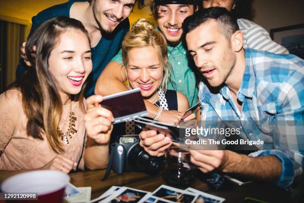 happy friends looking at photographs at table during party - souvenirs photos et images de collection