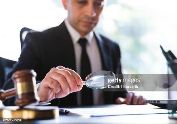man in black suit reading a legal document carefully using magnifying glass - legal system stock pictures, royalty-free photos & images