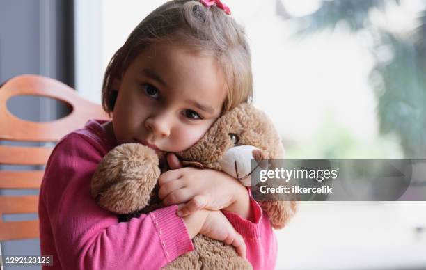 little child girl hugging her toy bear at home nearby window - sombre stock pictures, royalty-free photos & images