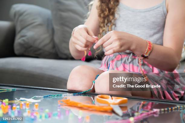 midsection of girl making bracelet while sitting on sofa at home - bracelet making stock pictures, royalty-free photos & images