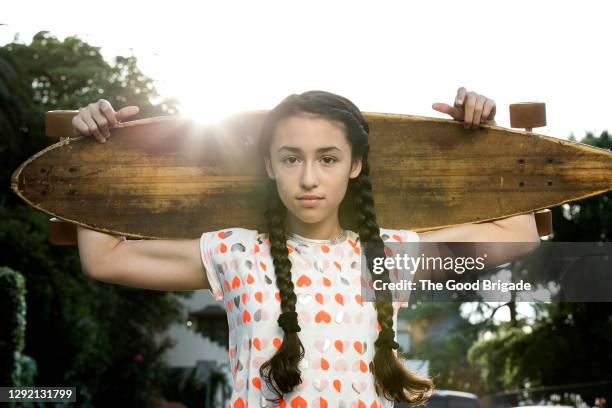 portrait of confident girl carrying skateboard on shoulders while standing outdoors during sunny day - leanincollection stock pictures, royalty-free photos & images