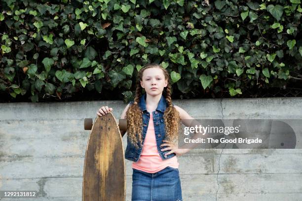 portrait of confident girl standing with skateboard against wall - pre adolescent child stock pictures, royalty-free photos & images