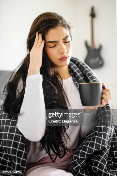sleeping young sick girl lying on a bed with cold and high fever and drinking tea - covid 19 symptoms stock pictures, royalty-free photos & images