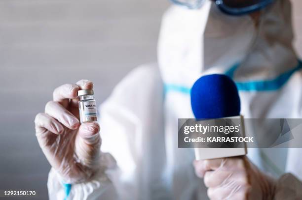 reporter in protective suit and microphone shows the covid 19 vaccine to the camera - science journalism stock pictures, royalty-free photos & images