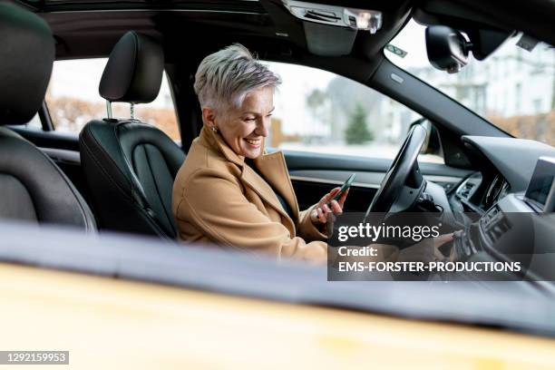 active bestager women is using smart phone to start a sharing car - green coat foto e immagini stock