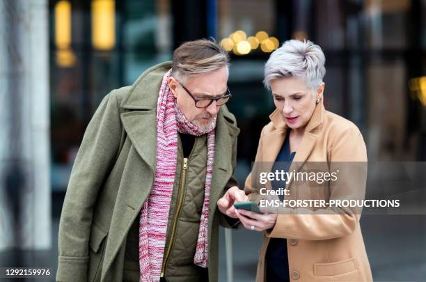 senior couple using smartphone while they are looking for a next sharing car - munich winter stock pictures, royalty-free photos & images