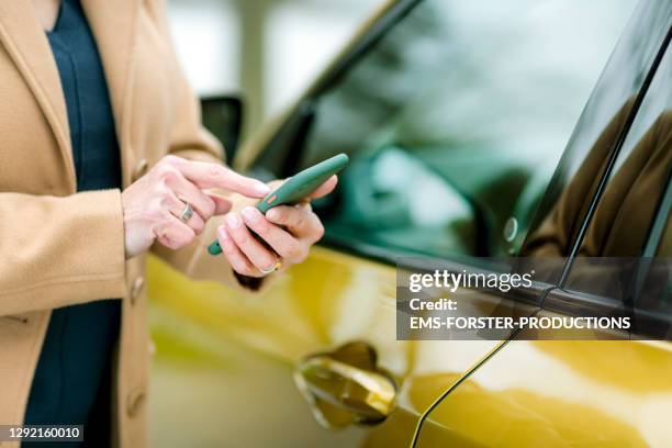 close up from a beautiful bestager women who is using smart phone to unlock a rental car - carsharing - car sharing stock pictures, royalty-free photos & images