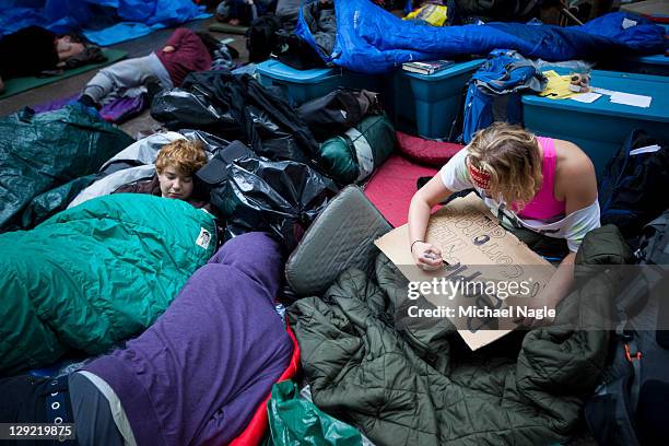 An "Occupy Wall Street" demonstrator makes a sign as others sleep in Zuccotti Park after marching in the financial district on October 14, 2011 in...