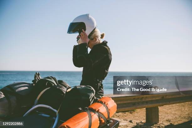 young woman putting on motorcycle helmet during road trip - sturzhelm stock-fotos und bilder