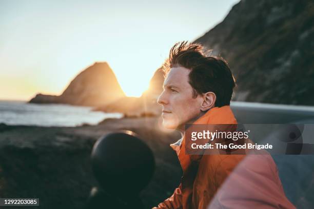side view of man looking at ocean during sunset - mare moto foto e immagini stock