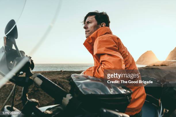 mature man wearing orange jacket sitting on motorcycle during sunset - adultes moto photos et images de collection