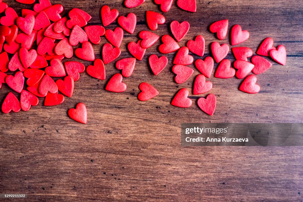 Valentines Day background with red hearts on a wooden table, top view. Red heart shaped candies on a wooden brown background. The concept of Valentines Day.