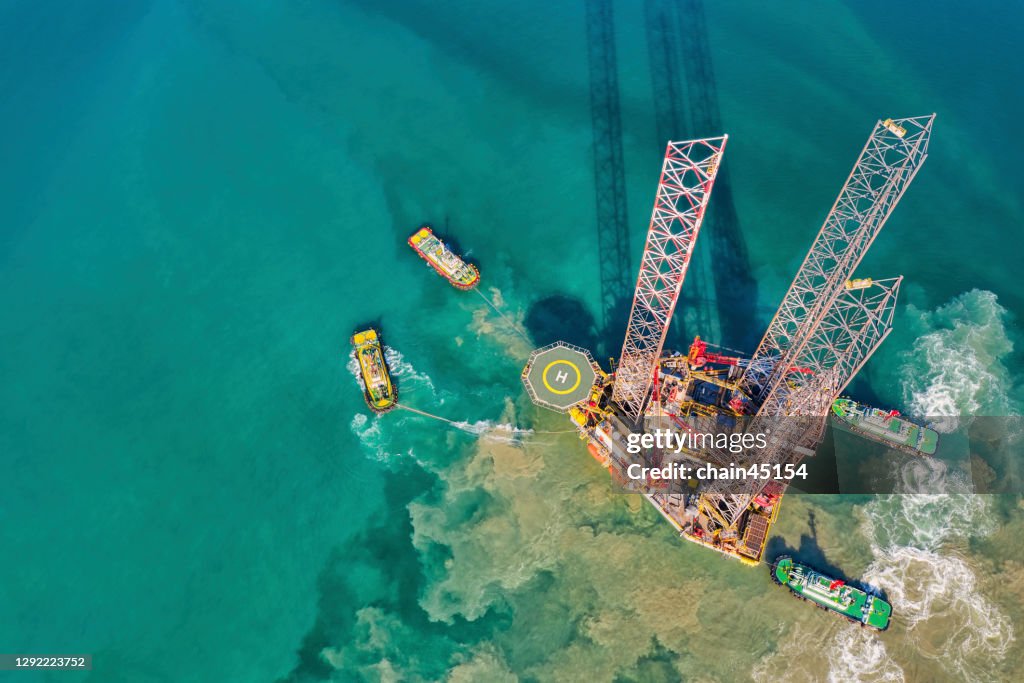 Aerial view of Drilling oil rig move operation at oil field industry with towing boat from shore in shallow water.