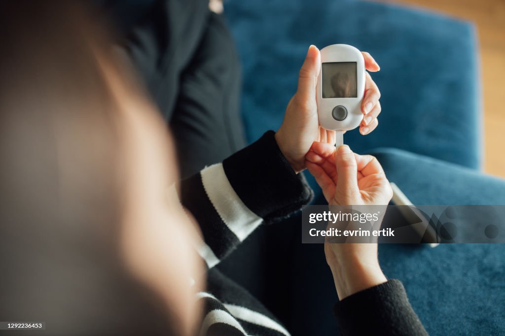 Diabetes checking blood sugar level. Woman using lancelet and glucometer at home