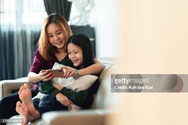 asian mother sharing screen time with her daughter - parental control stock pictures, royalty-free photos & images